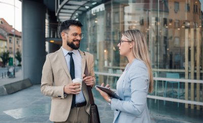 Two business professionals engaged in a casual conversation, standing in a modern office environment.