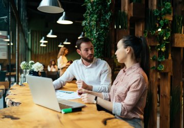 People discussing a plan while sitting on a table with an open laptop.