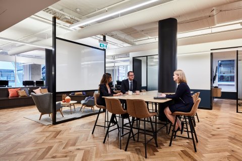 Three people around a meeting table in an open space.