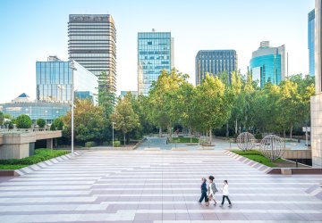 Tall real estate buildings in the back with persons walking through a park 