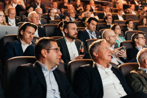 Audience seated in a conference hall attentively listening to presentations.