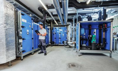 Technician monitoring HVAC machinery via tablet in an industrial maintenance setting.