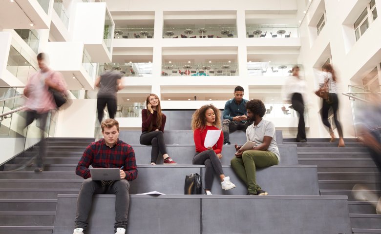 Higher education students sitting on the stairs in the hall of a building.