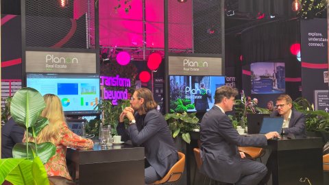 Visitors viewing software dashboards displayed on screens at the Planon Real Estate stand.