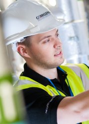 Maintenance professional in a safety vest and hard hat working on equipment in an industrial setting.