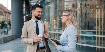 Two business professionals engaged in a casual conversation, standing in a modern office environment.