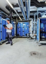 Technician monitoring HVAC machinery via tablet in an industrial maintenance setting.