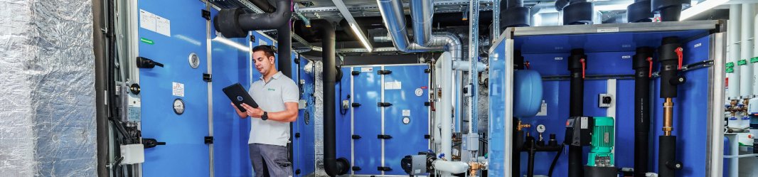 Technician monitoring HVAC machinery via tablet in an industrial maintenance setting.