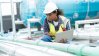 A maintenance technician inspects industrial piping with a laptop, wearing safety gear, in front of blue machinery.