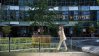Woman walking in front of real estate building with trees and plants.