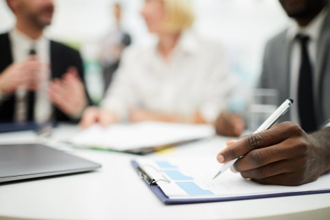 Focused shot of a clipboard as professionals discuss and take notes during a meeting.