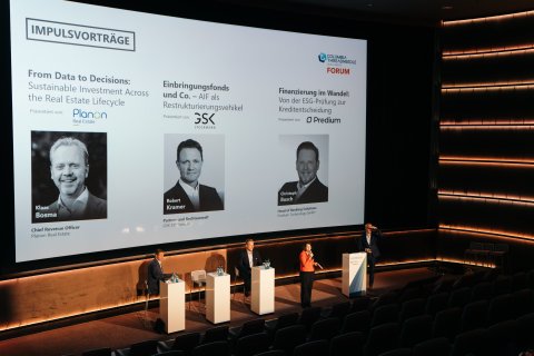 Conference stage showing multiple speakers and presentation slides during keynote sessions.