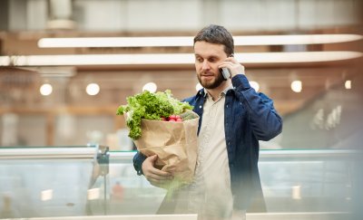 Man holding groceries when using his mobile device