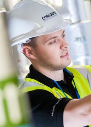 Maintenance professional in a safety vest and hard hat working on equipment in an industrial setting.
