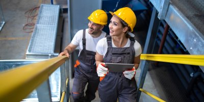 Two maintenance workers climbing stairs in a factory.