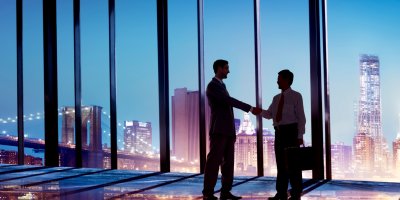Two businessmen shaking hands in glass office building.