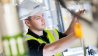 Maintenance professional in a safety vest and hard hat working on equipment in an industrial setting.