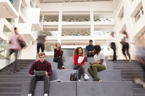 Higher education students sitting on the stairs in the hall of a building.