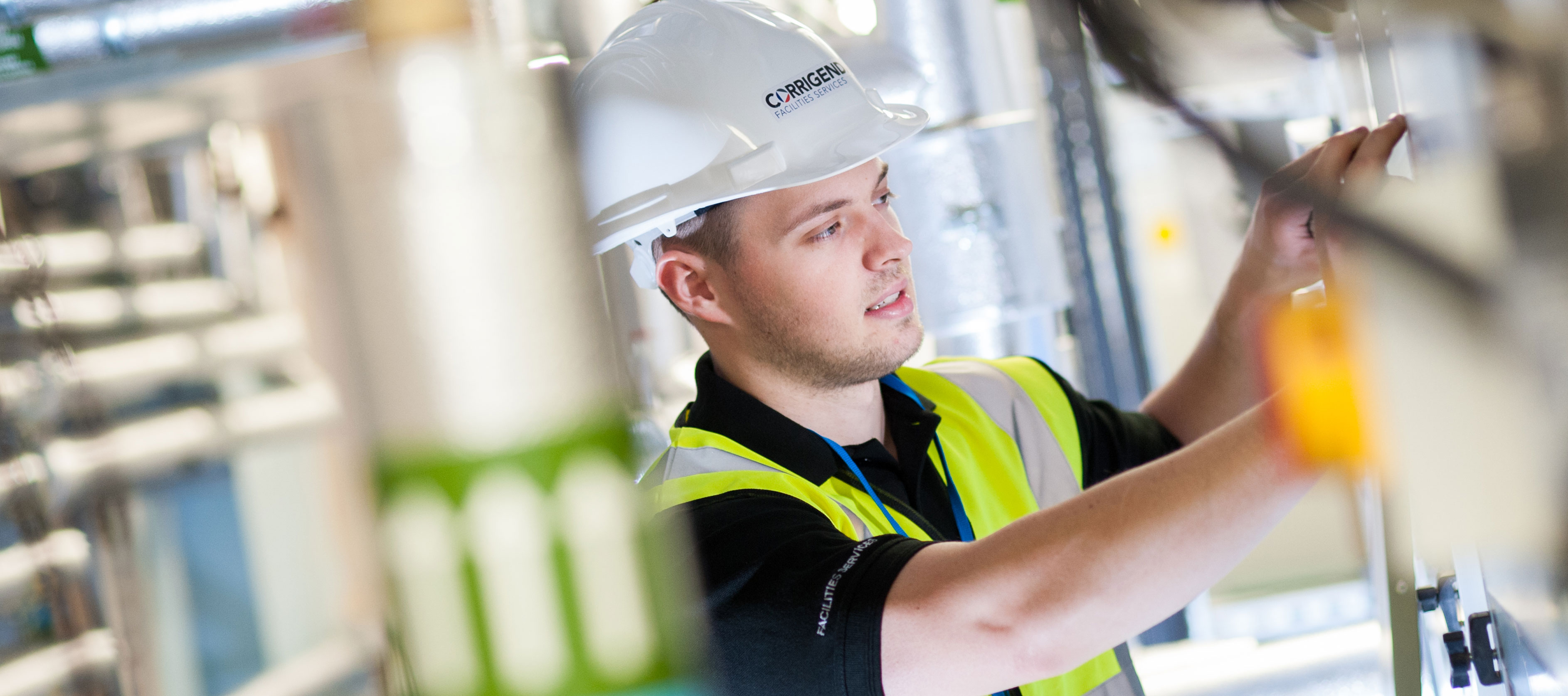 Maintenance professional in a safety vest and hard hat working on equipment in an industrial setting.