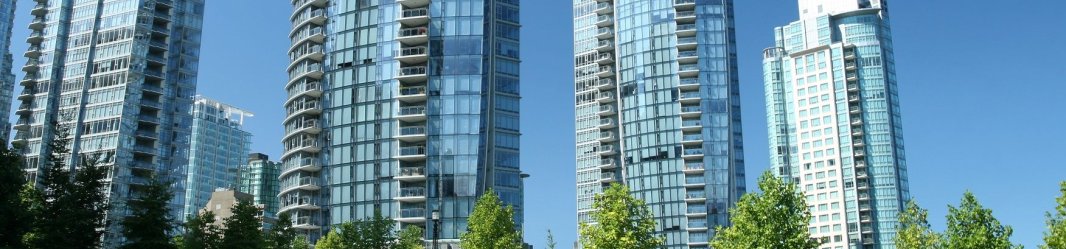 Multiple tall buildings with many windows behind a green area.