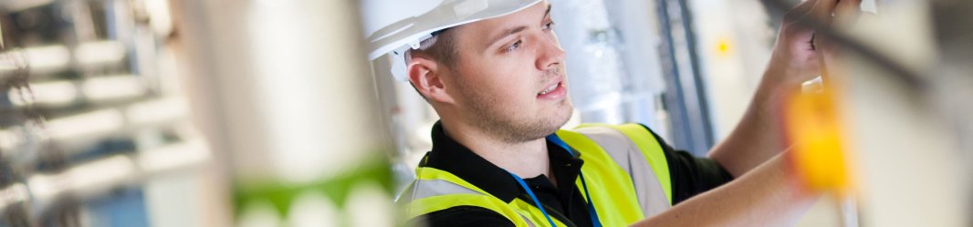 Maintenance professional in a safety vest and hard hat working on equipment in an industrial setting.