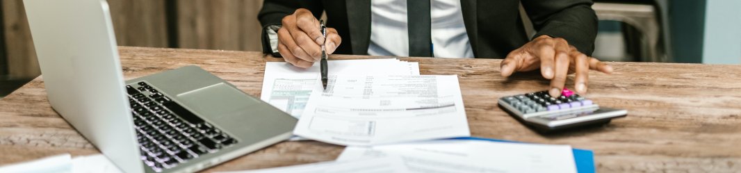 A man in a black suit working on financial data with a calculator.