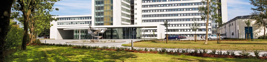 A big white office building with large glass windows, set among trees and green surroundings.