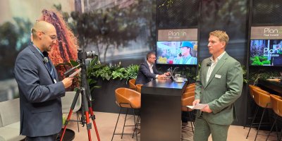Video interview being recorded at the Planon Real Estate stand with a tripod-mounted camera and exhibition displays visible.