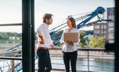 Two business professionals standing on a balcony, engaged in a thoughtful discussion, with a city skyline in the background.