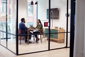 Two people in a meeting room inside a workspace with glass walls..