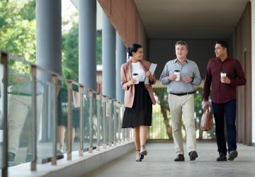 Business people walking and drinking coffee on the outside of a building.