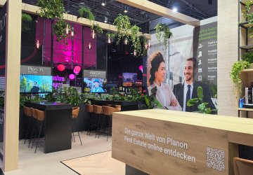 Empty Planon Real Estate exhibition stand with seating areas, digital displays and plant decorations.