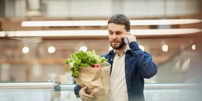 Man holding groceries when using his mobile device
