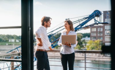 Two business professionals standing on a balcony, engaged in a thoughtful discussion, with a city skyline in the background.