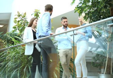 Young people brainstorming while standing against a glass railing.