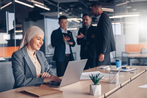 Businesswoman in hijab working on laptop in modern office.