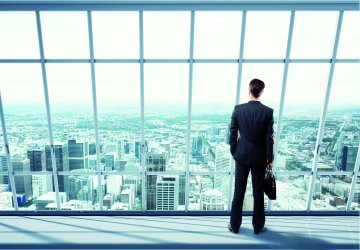 Businessman standing in front of a large window in an office looking out.