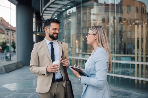 Two business professionals engaged in a casual conversation, standing in a modern office environment.