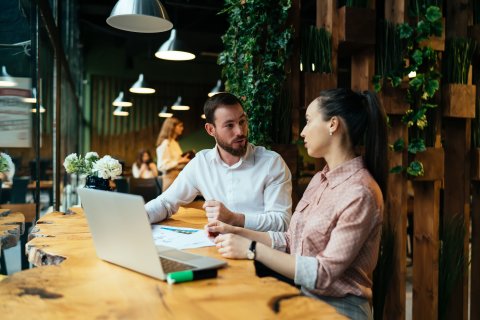 People discussing a plan while sitting on a table with an open laptop.