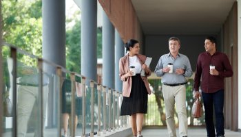Business people walking and drinking coffee on the outside of a building.