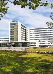 A big white office building with large glass windows, set among trees and green surroundings.