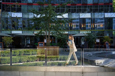 Woman walking in front of real estate building with trees and plants.