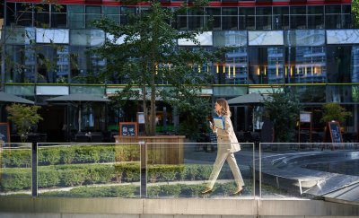 Woman walking in front of real estate building with trees and plants.
