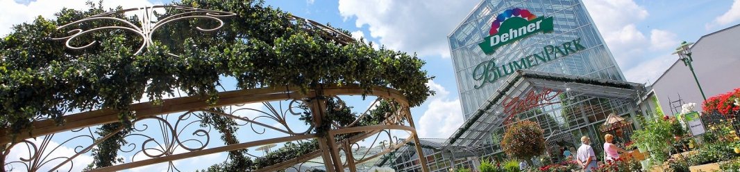 Dehner Blumenpark's lush plant displays and metal gazebo under a bright blue sky with white clouds.