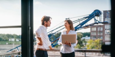Two business professionals standing on a balcony, engaged in a thoughtful discussion, with a city skyline in the background.