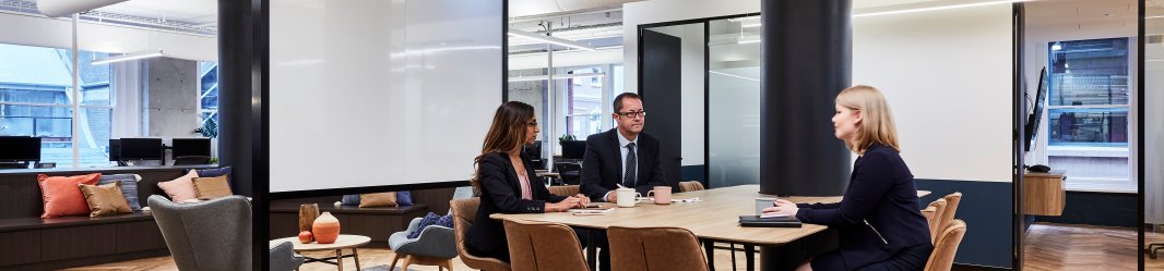 Three people around a meeting table in an open space.