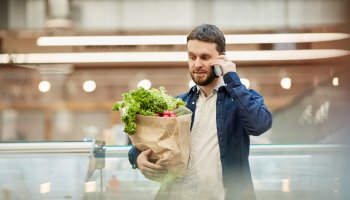 Man holding groceries when using his mobile device