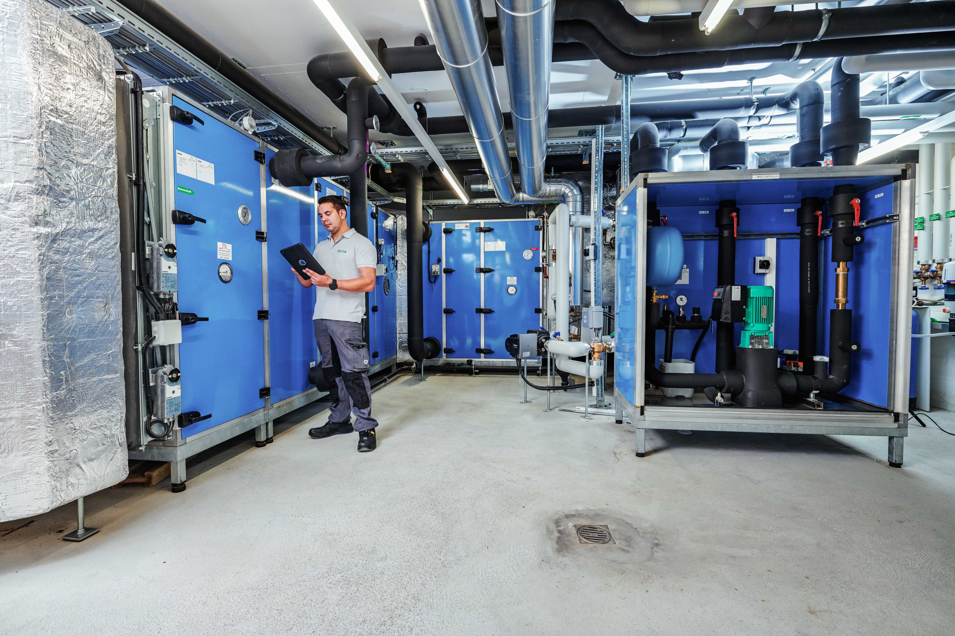 Technician monitoring HVAC machinery via tablet in an industrial maintenance setting.