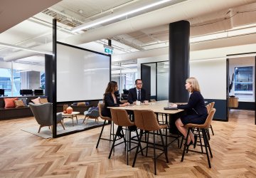 Three people around a meeting table in an open space.