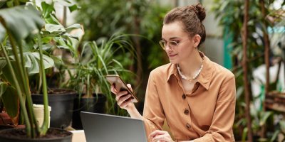 Young smiling businesswoman in brown blouse scrolling in mobile phone.